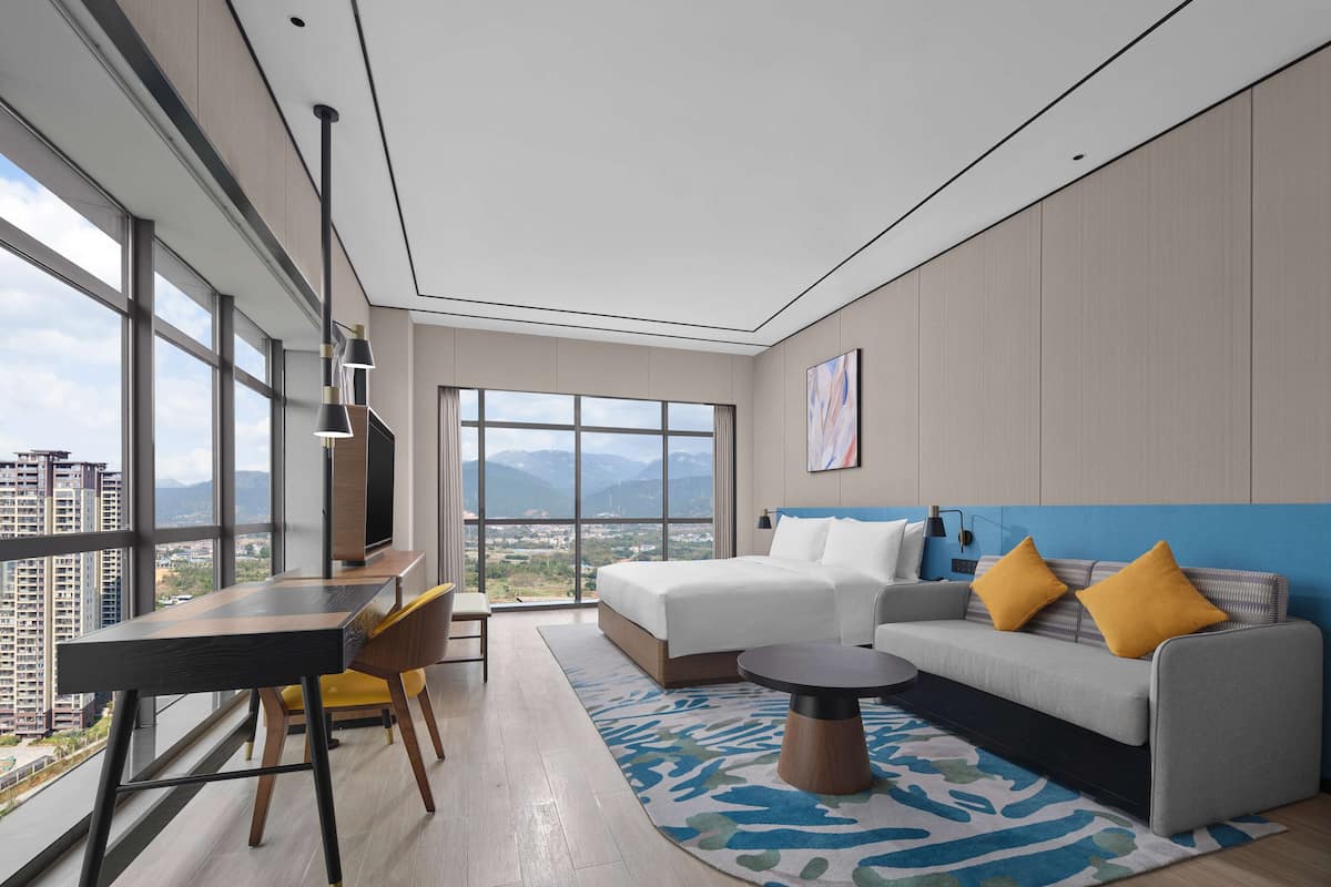 Een moderne hotelkamer met een groot raam, een bank, een eettafel en een televisie.