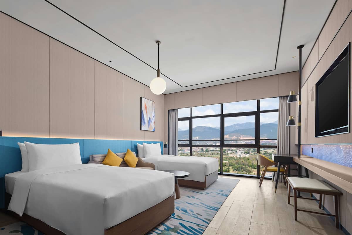 Een moderne hotelkamer met twee bedden, een groot raam met uitzicht op de stad, een flatscreen televisie en een klein bureau.