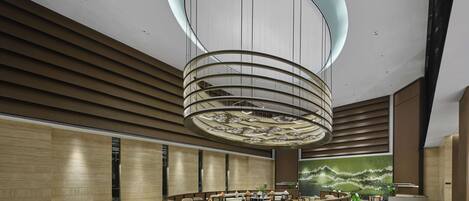 A modern lobby with a central circular reception desk, a large chandelier, and a mural on the wall.