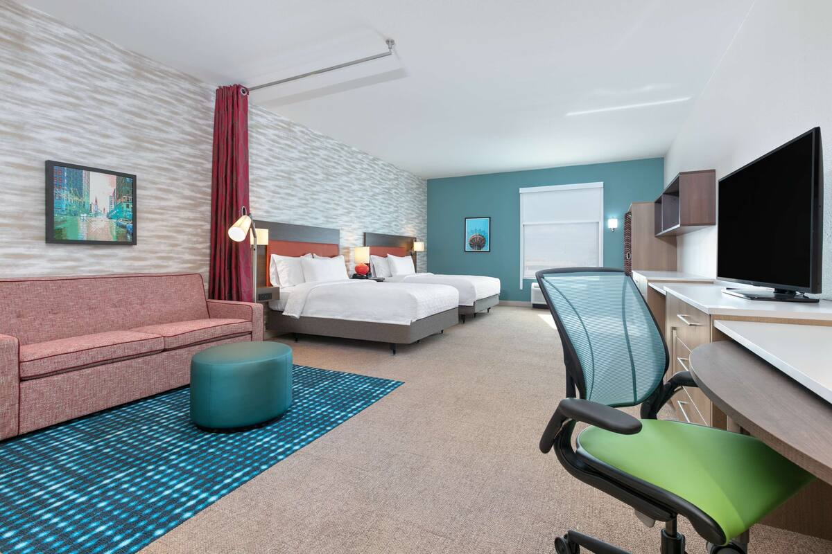 A hotel room with a bed, a desk, a TV, a chair, a sofa, and a patterned rug.