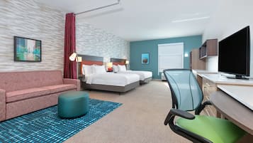 A hotel room with a bed, a desk, a TV, a chair, a sofa, and a patterned rug.