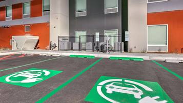 A parking area with electric vehicle charging stations and a building with orange and grey exterior walls.