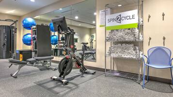 Ett gym med träningsutrustning, en spegel och ett väggmonterat hyllsystem med handdukar.