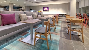 A modern lounge area with a sofa, tables, chairs, and a colorful carpet. - Home2 Suites By Hilton Tulsa Airport (Tulsa)