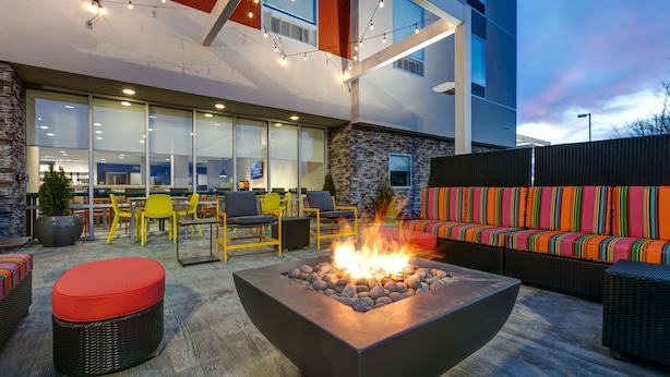 An outdoor seating area with a fire pit, yellow chairs, and a colorful sofa. - Home2 Suites By Hilton Tulsa Airport (Tulsa)