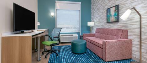 Une chambre d’hôtel équipée d’un bureau, d’une télévision, d’un canapé, d’une chaise, d’une lampe et d’un tapis à motifs.