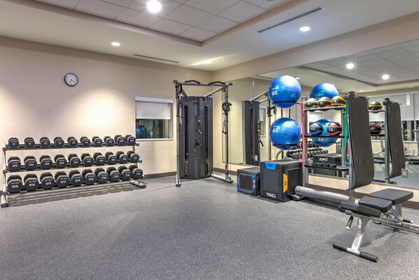 A gym with weightlifting equipment, dumbbells, and exercise balls.