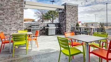 Terrassa a l'exterior amb parets de pedra, una barbacoa i caires i taules de colors.