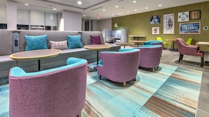 A modern lounge area with seating, tables, and artwork on the walls. - Home2 Suites By Hilton Tulsa Airport (Tulsa)