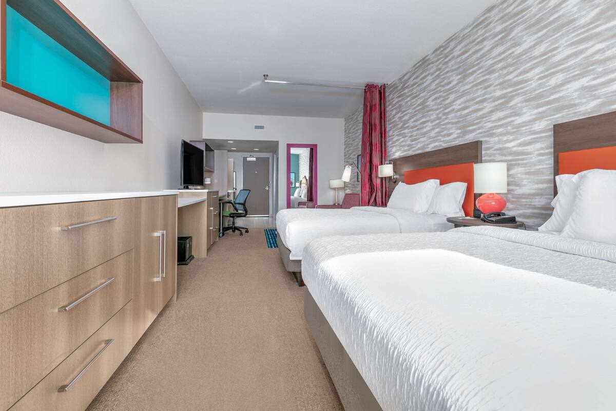 A hotel room with a bed, a desk, a chair, a TV, and a bathroom door.