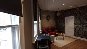 Ein gemütliches Wohnzimmer mit einem roten Sofa, einem kleinen runden Tisch und einem Essbereich mit Tisch und Stühlen.