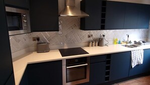 Eine moderne Küche mit dunklen Schränken, einer Edelstahl-Dunstabzugshaube, einer eingebauten Mikrowelle, einem Toaster und einem Spülbecken mit einem Handtuch am Wasserhahn.