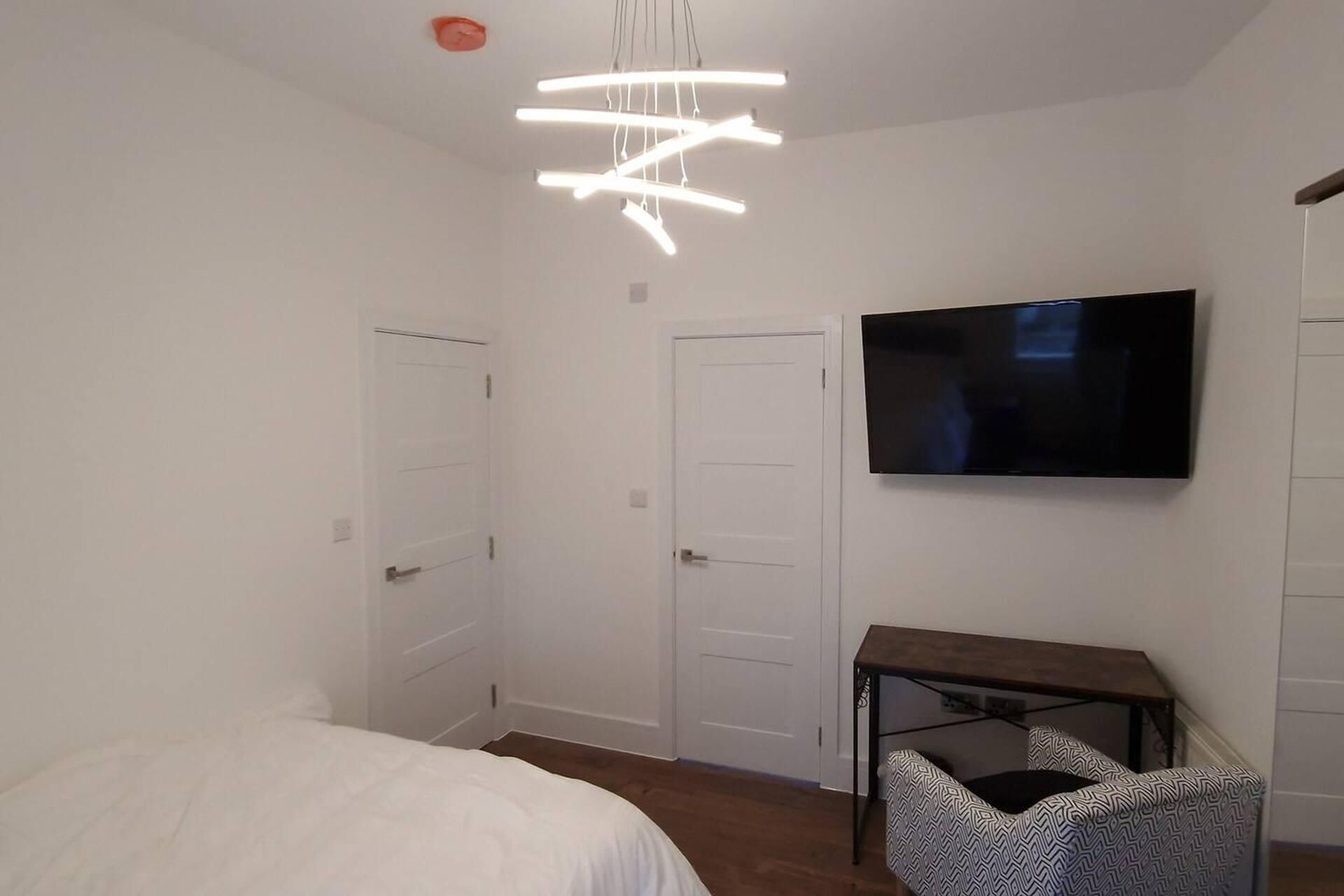 A bedroom with a bed, a desk, a chair, a TV, and a ceiling light fixture.