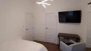 Ein Schlafzimmer mit Bett, Schreibtisch, Stuhl, Fernseher und einer Deckenleuchte.