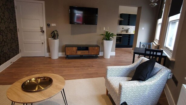 Ein Wohnzimmer mit einer Couch, einem Couchtisch, einem Fernseher und einer Küche im Hintergrund.