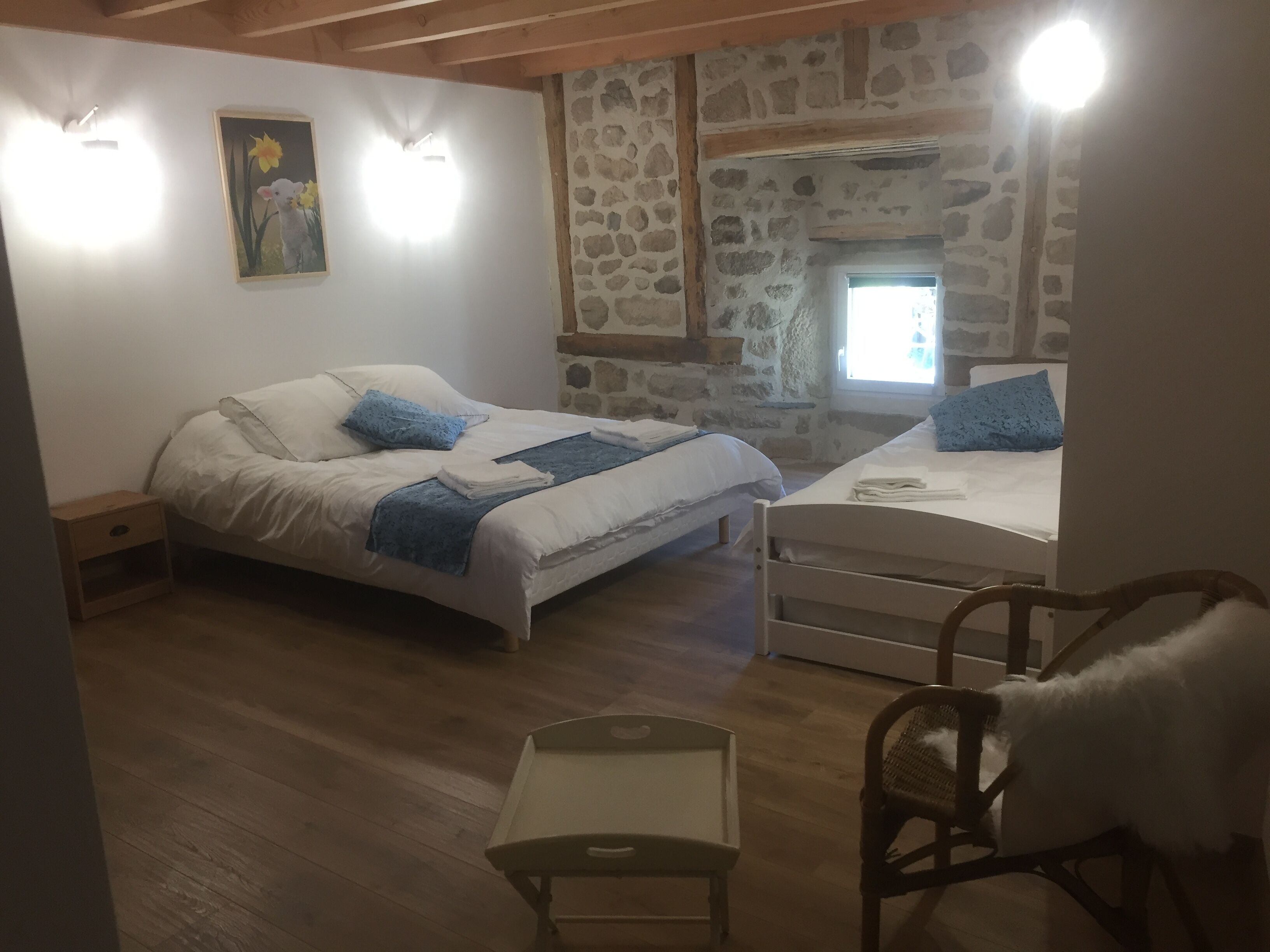 Ein Schlafzimmer mit Bett, Sessel, Nachttisch, kleinem Tisch und einer Steinwand.