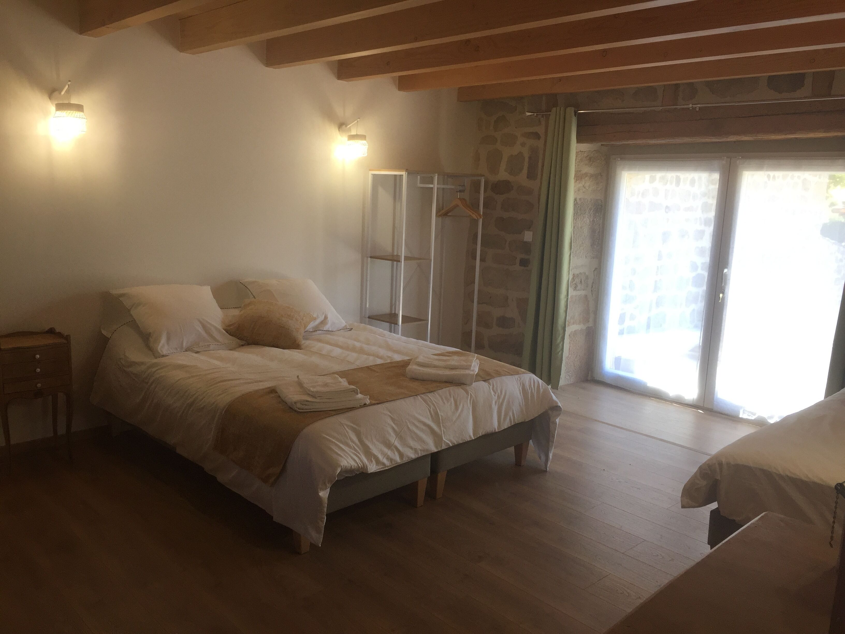 A bedroom with a bed, wooden headboard, bedside tables, a stone wall, and a sliding glass door.