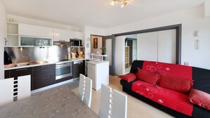 A modern kitchen with white cabinets, a dining area with a table and chairs, and a red sofa in the living room.