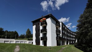 A modern multi-story building with balconies, a paved pathway, and a grassy area.