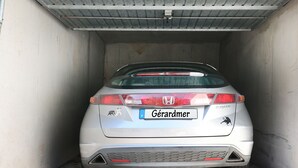 A silver Honda car parked inside a garage with a metal roof and concrete walls.