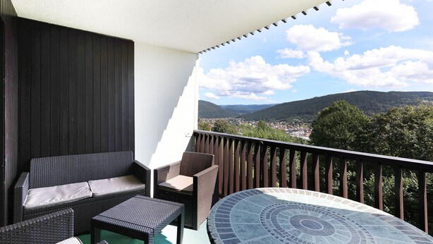 A balcony with wicker furniture, a tiled table, and a view of a town and mountains.