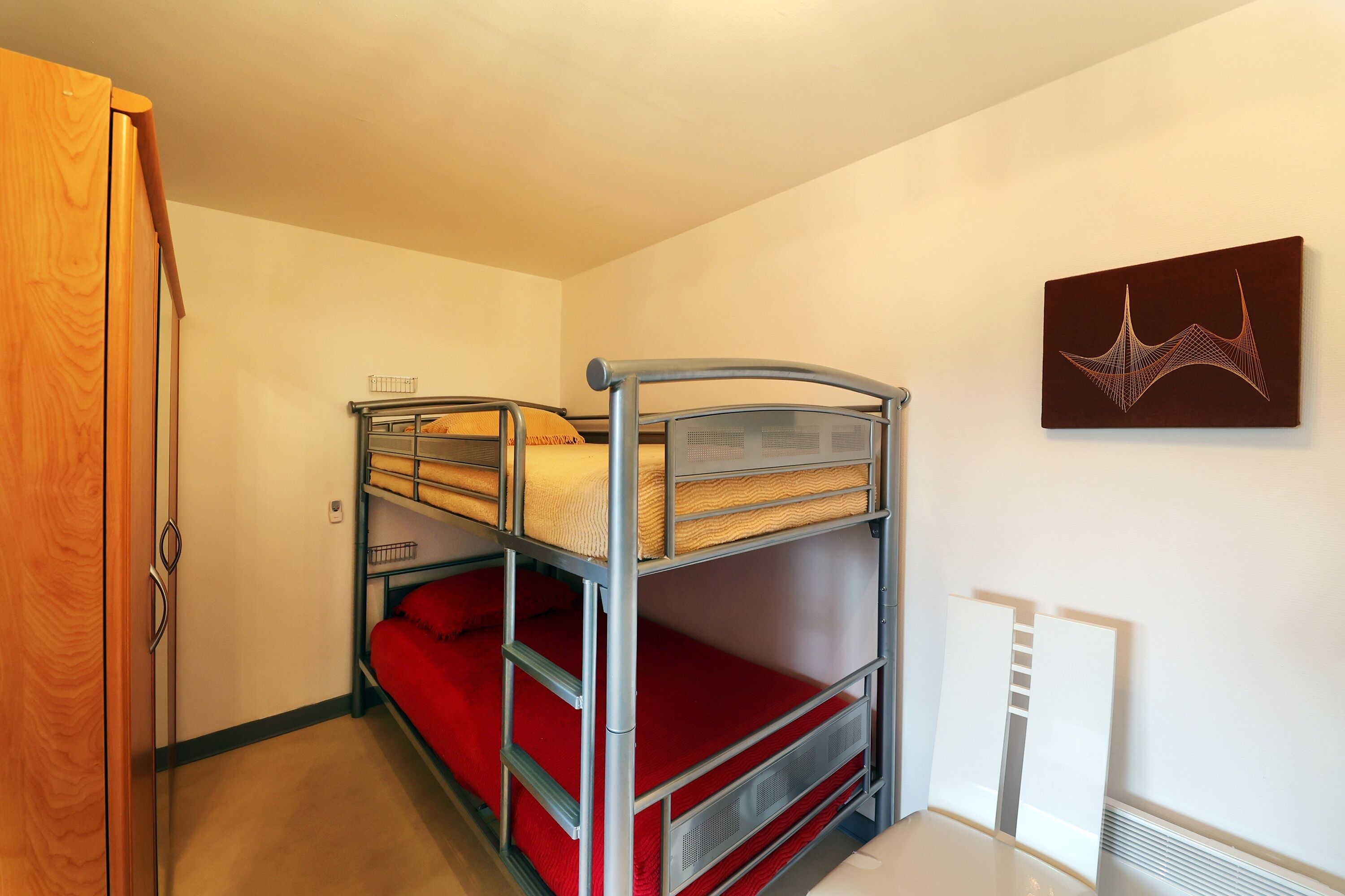 A bunk bed room with a wooden wardrobe and a wall-mounted artwork.