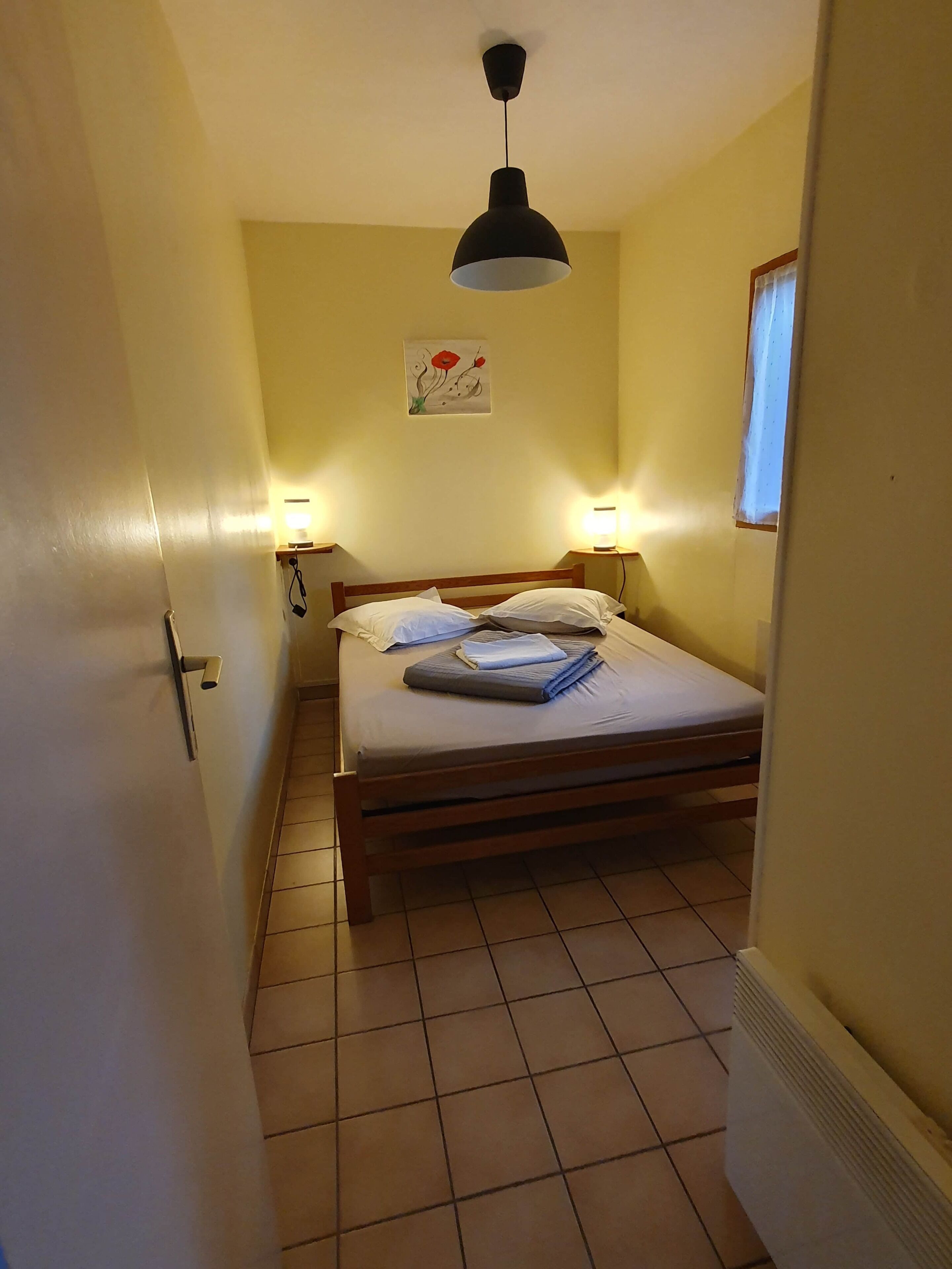 Une chambre à coucher avec un lit, deux lampes de chevet, un tableau au mur et une fenêtre avec des rideaux.