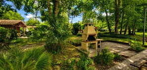 Ein rustikaler Außenbereich mit einem Grill aus Naturstein, umgeben von üppigem Grün und einer Holzpergola.