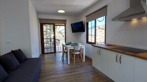 A compact kitchen with a dining area, a sofa, and a TV mounted on the wall.