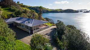 A house with a large patio, surrounded by lush greenery and a view of a calm lake. - Seascape Point - Mahinepua Bay Clifftop Retreat (Mahinepua Bay)