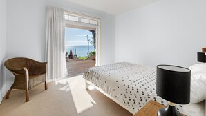 A bedroom with a bed, a chair, a lamp, and a view of the sea through a large window. - Seascape Point - Mahinepua Bay Clifftop Retreat (Mahinepua Bay)