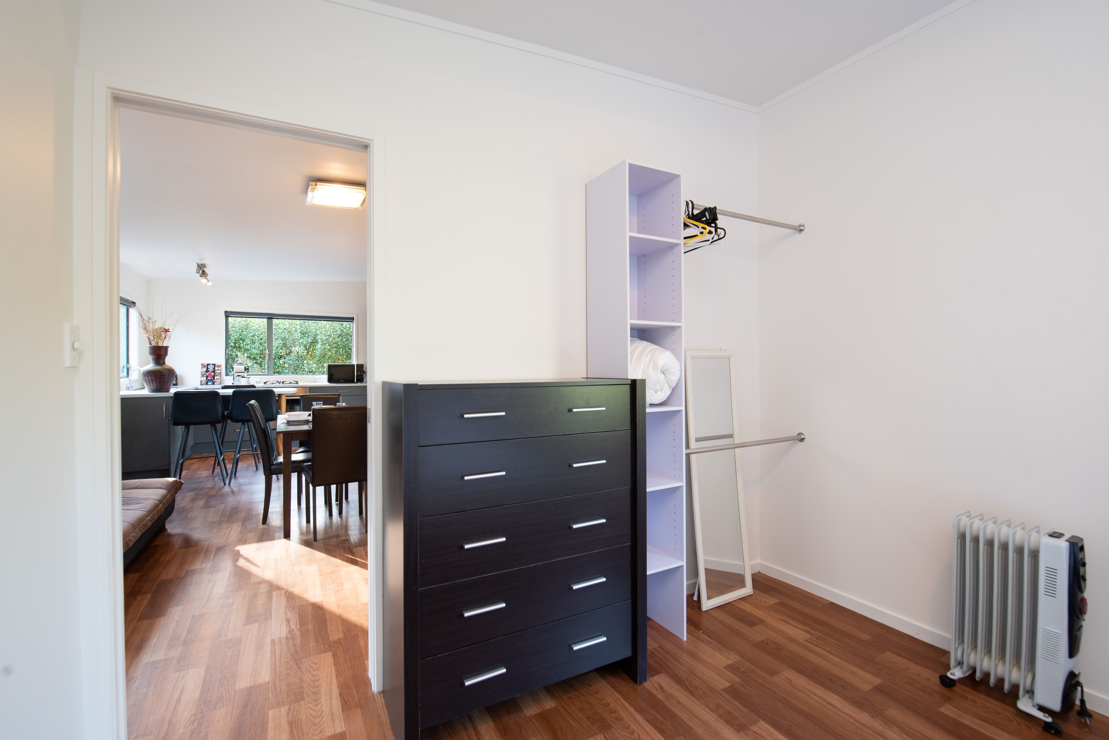 A modern room with a black dresser, a white shelving unit, and a radiator.