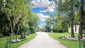 A gravel driveway leading to a house surrounded by lush greenery and trees. - Tree Tops Everything is brand new (St. Augustine)