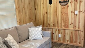 A room with a wooden paneled wall, a grey sofa with patterned cushions, and a wooden floor.