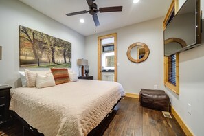 Une chambre à coucher avec un grand lit, un ventilateur de plafond, un tableau, un miroir et un plancher en bois.