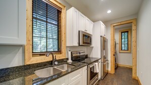 A kitchen with white cabinets, a granite countertop, stainless steel appliances, and a window with blinds. - Lakefront Gem w/ Fire Pit in Chinquapin Resort! (Glenville)