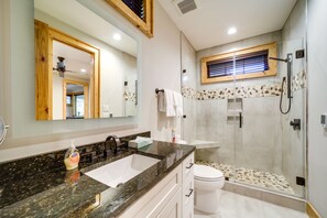 Une salle de bain moderne avec un comptoir en granit, un lavabo blanc, une douche à parois de verre et une fenêtre à cadre en bois.