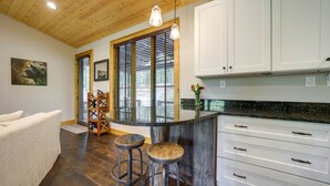 A kitchen with wooden flooring, white cabinets, a bar area with stools, and a large window with blinds. - Lakefront Gem w/ Fire Pit in Chinquapin Resort! (Glenville)