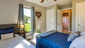 A bedroom with two beds, a window with curtains, a heart-shaped decoration, and a view of the outdoors. - Tranquil Cottage in Virginia Countryside w/ Pond! (Midlothian)