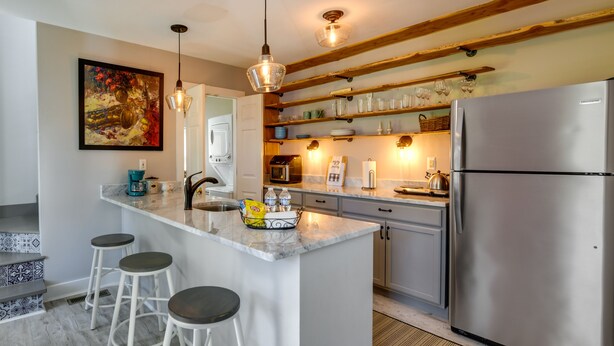 A modern kitchen with a central island, bar stools, stainless steel appliances, and a decorative painting. - Tranquil Cottage in Virginia Countryside w/ Pond! (Midlothian)