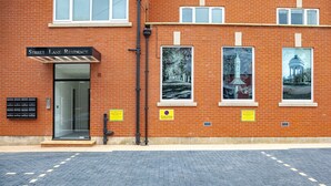 A brick building with a sign reading "Street Lane Residence." There are three posters on the wall, two of which depict trees and one of a gazebo. A "Private Parking Residents Only" sign is visible.