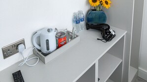 A hotel minibar with a kettle, tea, water bottles, a vase with sunflowers, and a remote control.