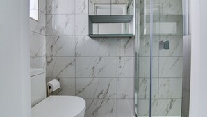 A bathroom with a toilet, a glass shower enclosure, and marble tiles.