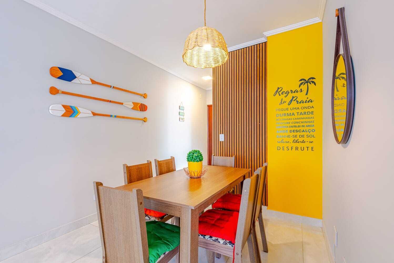 A dining area with a wooden table, chairs, a hanging light fixture, and a wall with a yellow accent and a decorative item.