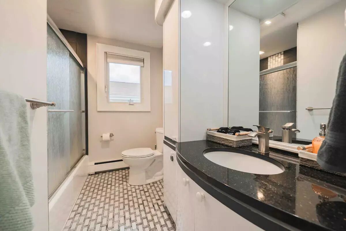 A bathroom with a white toilet, a black sink, a mirror, and a shower area.