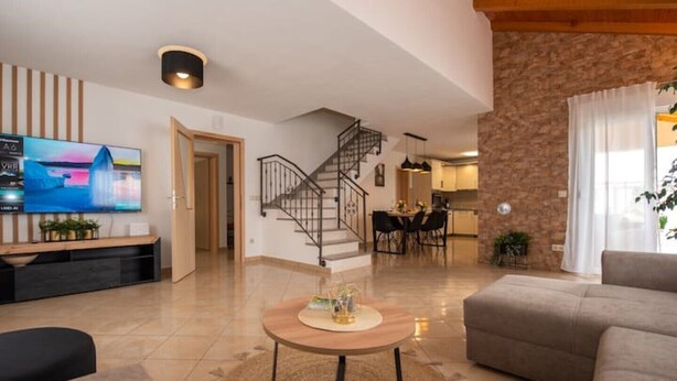 Un salon moderne avec un téléviseur, une table basse ronde et un escalier menant à la cuisine.