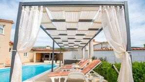 Un espace extérieur abrité comprenant une piscine, des chaises longues et une structure en forme de pergola.