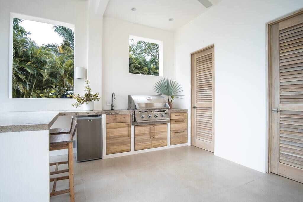 Una cocina moderna con una parrilla empotrada, armarios de madera y vistas a exuberante vegetación a través de amplios ventanales.