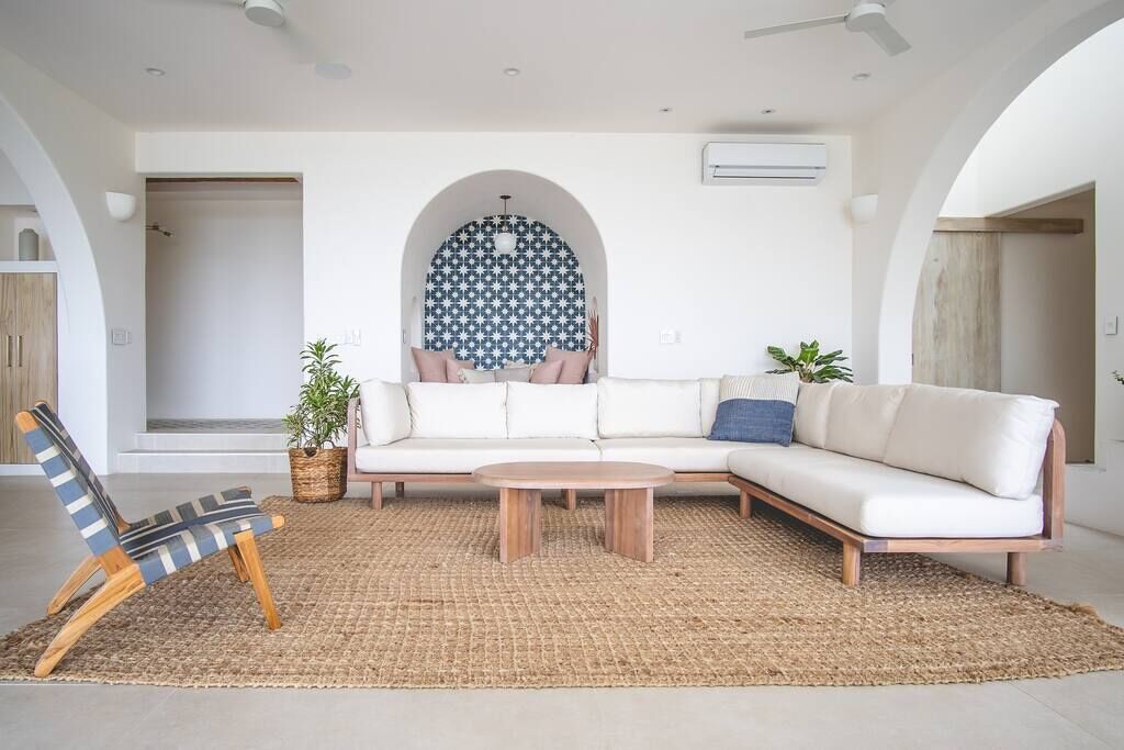 A modern living room with a white sofa, a striped chair, and a coffee table. There is a patterned wall and a plant in the corner.