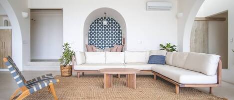 A modern living room with a white sofa, a striped chair, and a coffee table. There is a patterned wall and a plant in the corner.